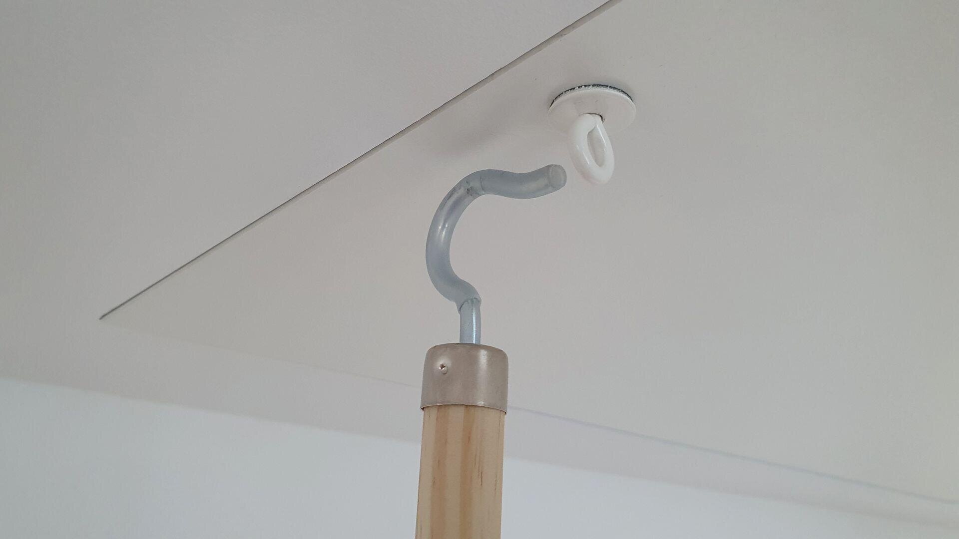 Eine Holzstange mit einem gebogenen Metallhaken wird verwendet, um eine Deckenluke herunterzuziehen, indem man sie an einer weißen Schlaufe einhakt, die an der Lukentür befestigt ist.