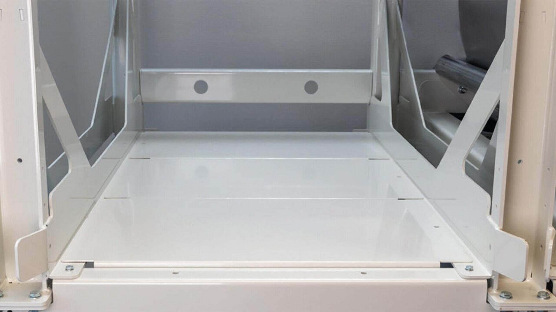 A close-up view of an empty, white metal bunk bed frame, showing the lower bunk platform with supports and structural beams on the sides.
