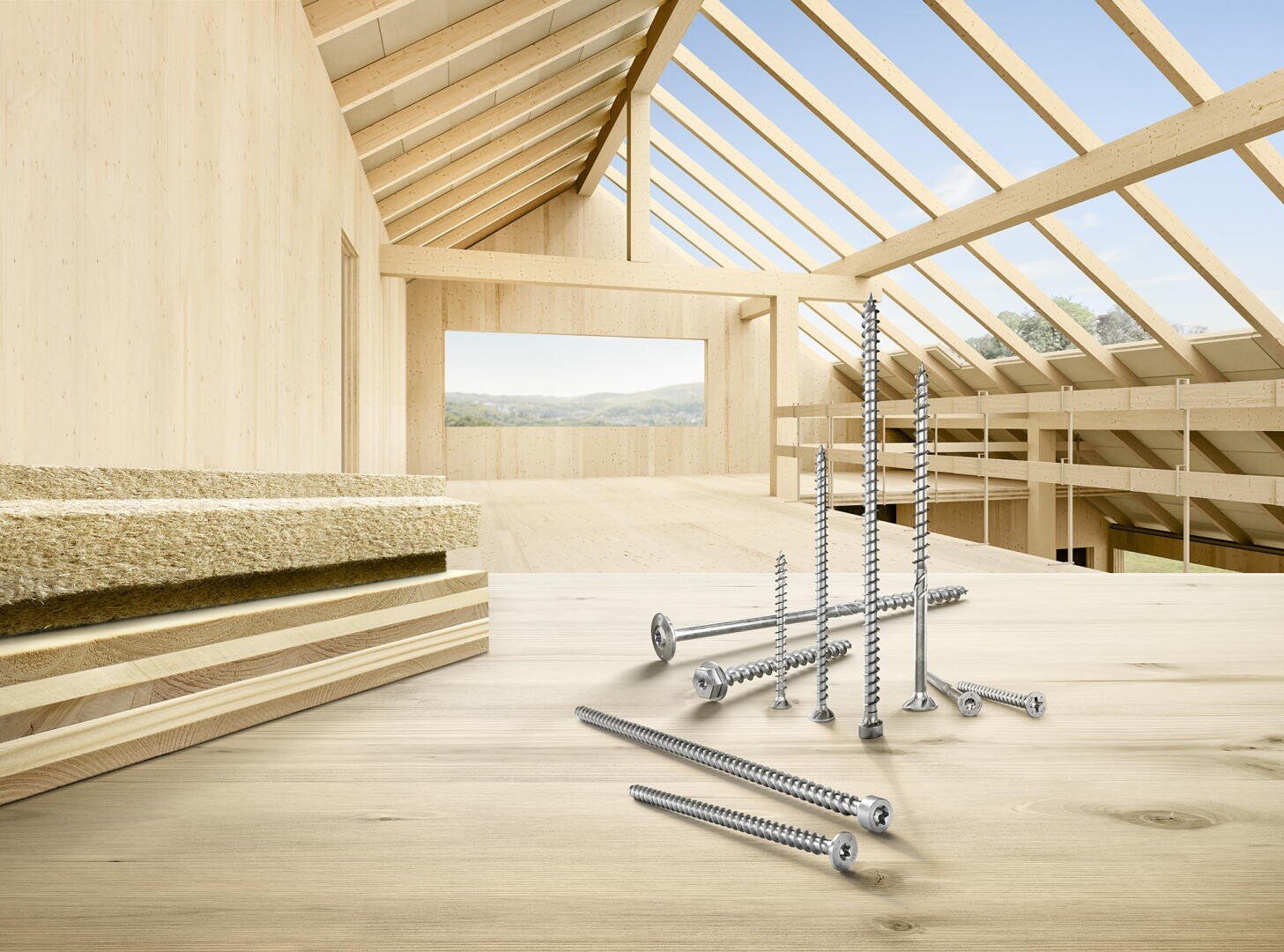 In a bright, unfinished wooden building with exposed beams and large windows looking out, several metal screws and layers of building materials are displayed on a wooden surface.