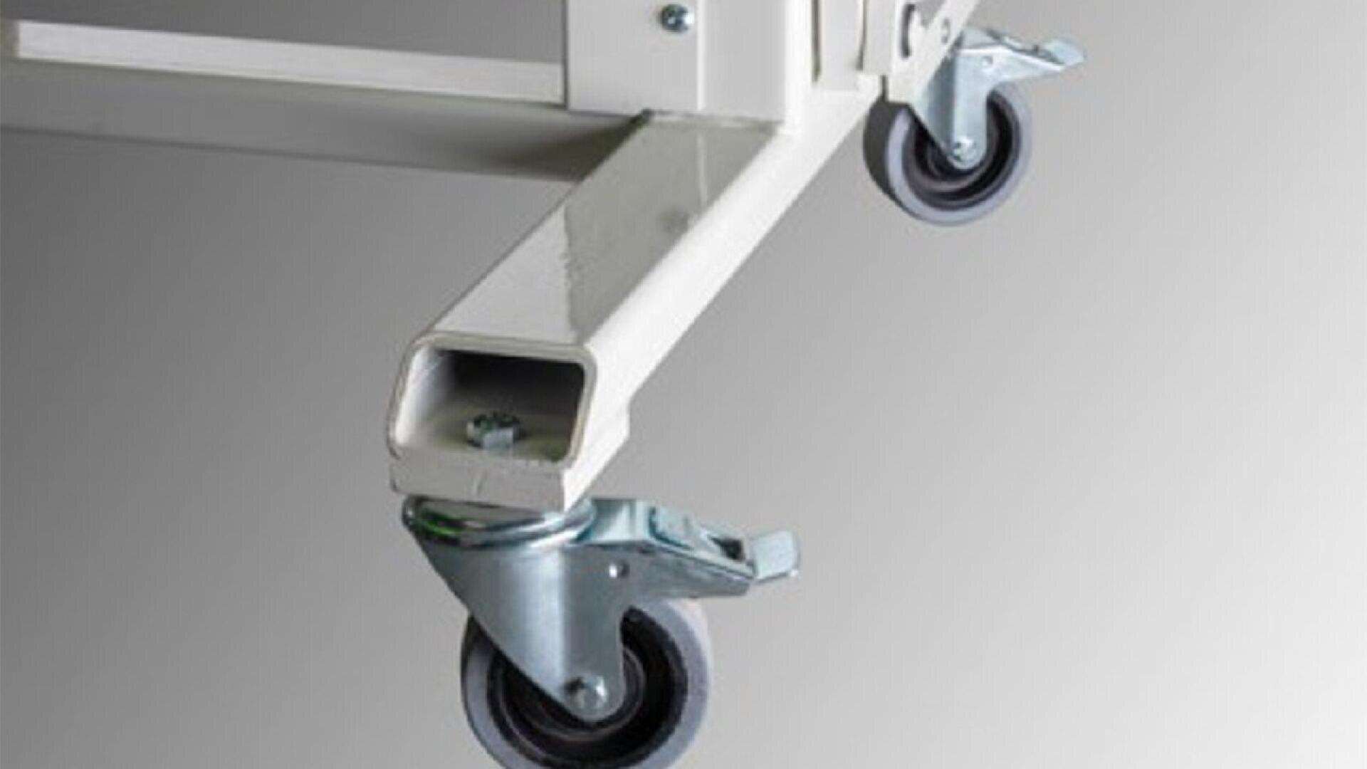 Close-up of two metal caster wheels attached to the bottom of a white metal frame, against a plain grey background.