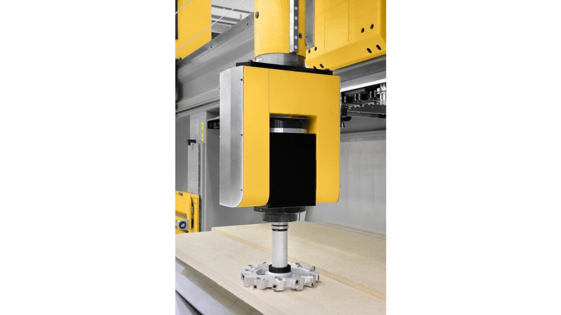 A close-up view of a yellow and black industrial CNC machine head with a cutting tool positioned above a flat sheet of material, ready for automated machining.