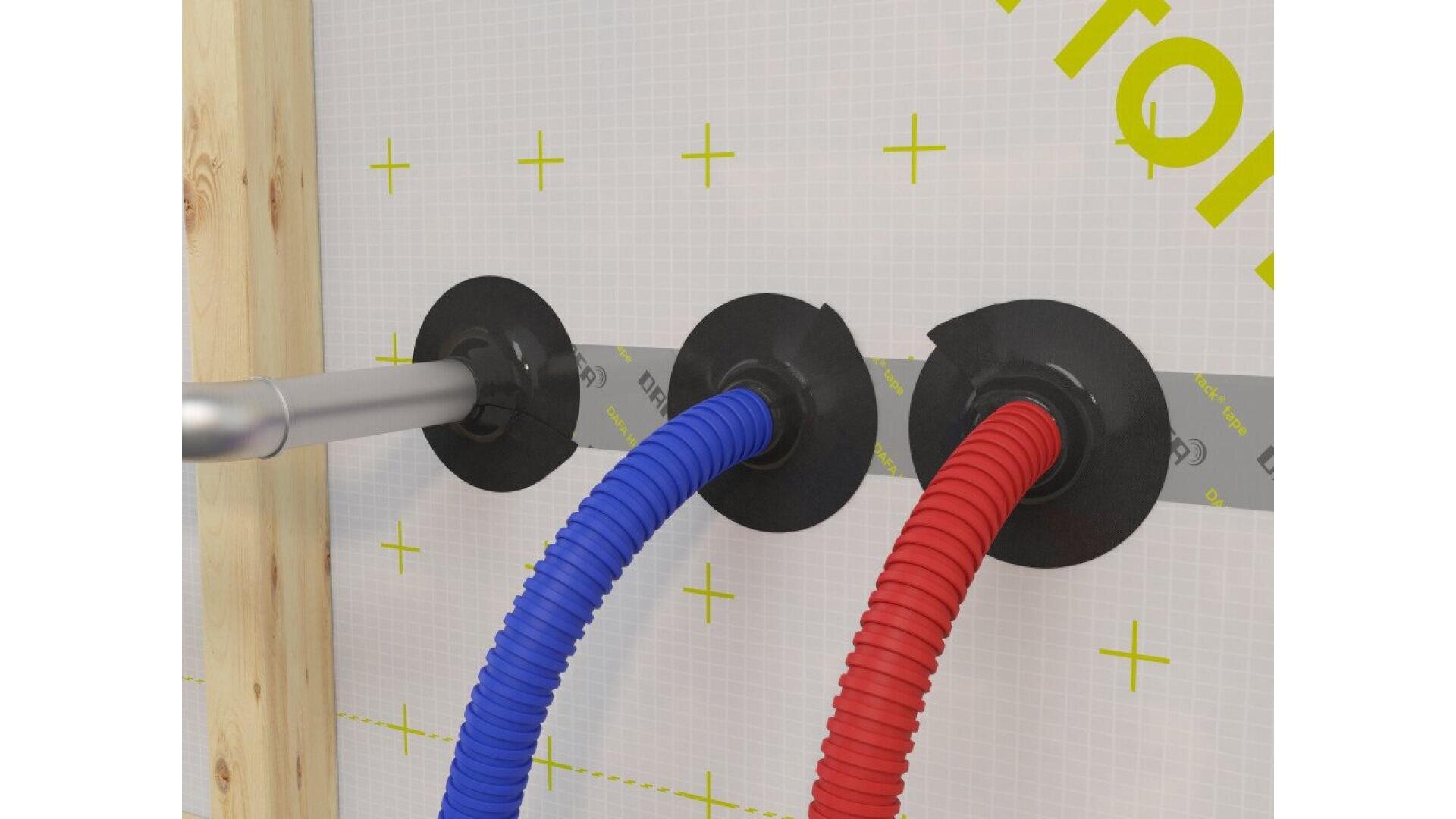 Three corrugated pipes—gray, blue, and red—are inserted through a wall with black sealing gaskets and tape, mounted on a grid-patterned surface with yellow markings.