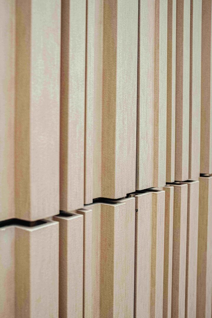A close-up of a modern wall with vertical, rectangular beige panels arranged in a repeating pattern, creating a textured and geometric look.