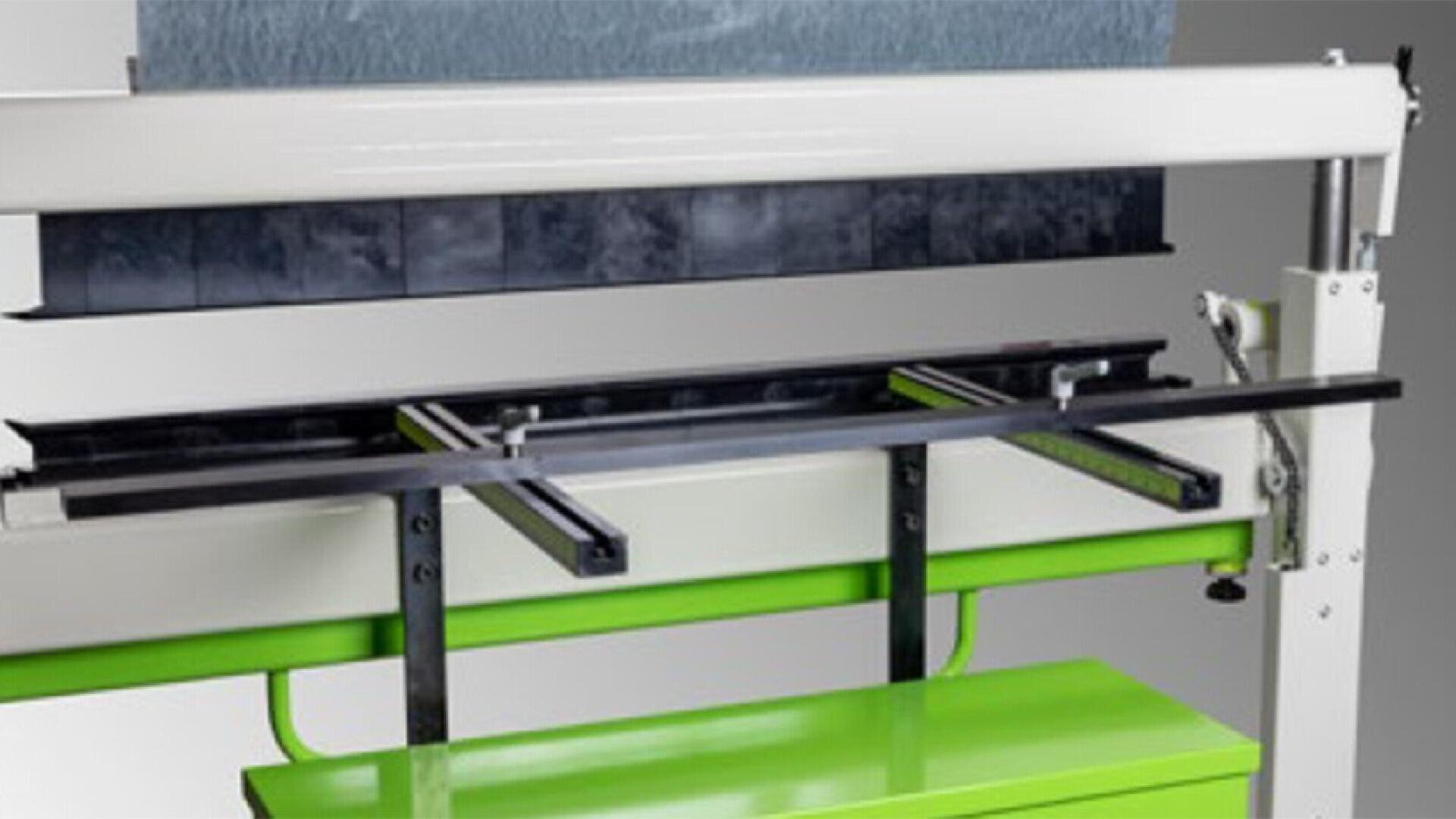 Close-up of a metal sheet bending machine with a white, black, and green frame, showing the bending bar and support arms. The machine is partially open, revealing its internal components.