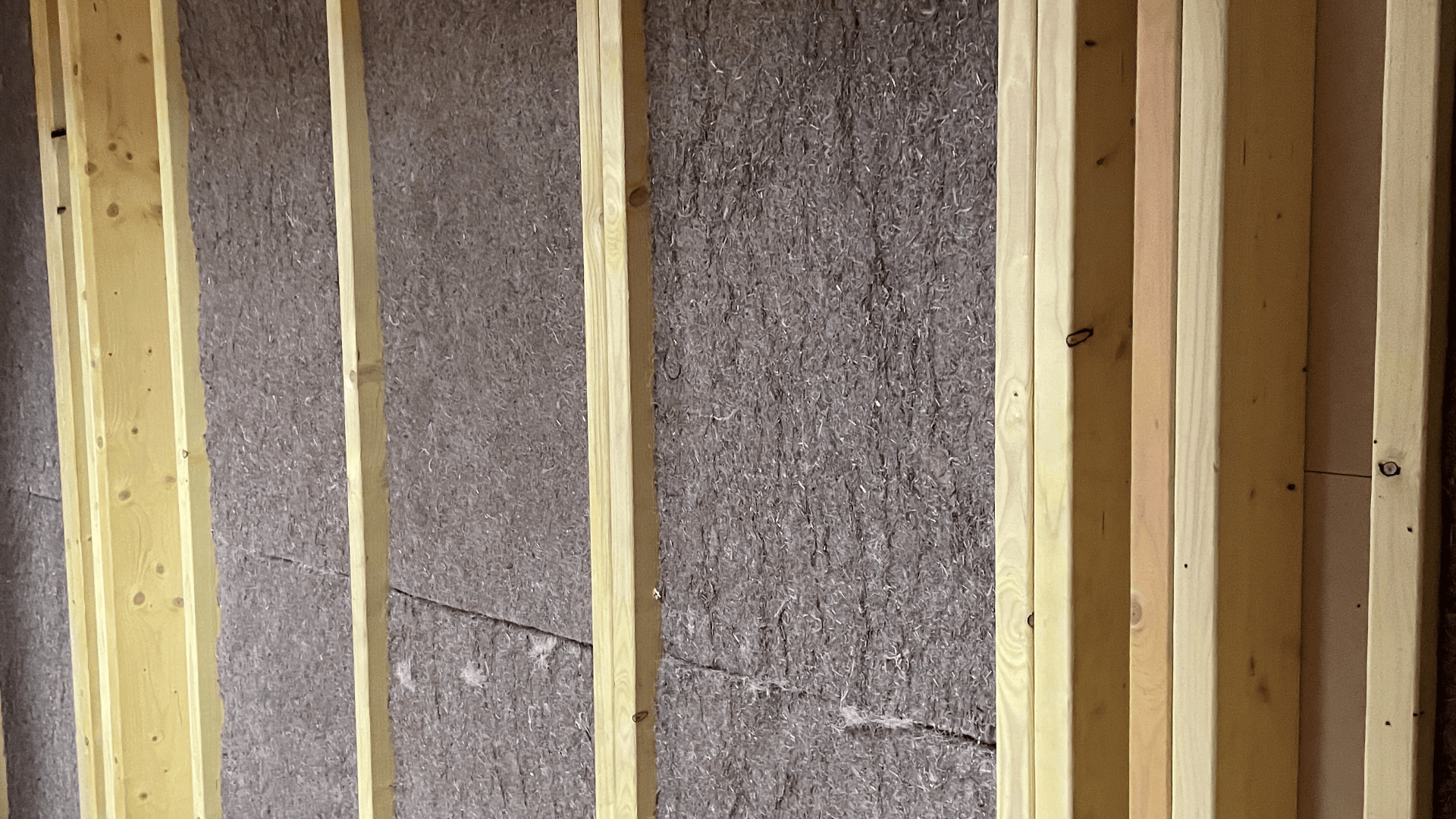 Holzwandpfosten mit dazwischen angebrachten grauen Dämmplatten zeigen eine im Bau befindliche, unfertige Innenwand.