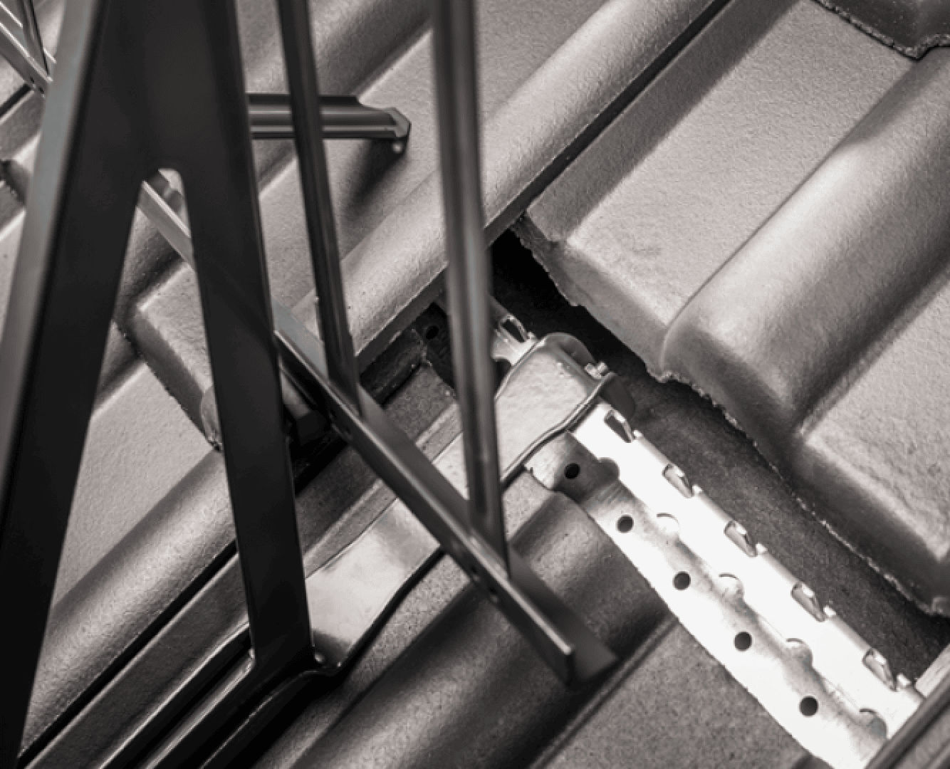 Nahaufnahme einer Metalldachkonstruktion, die auf grauen Dachziegeln installiert ist, und die Metallhalterungen und -träger zeigt, die an der Dachoberfläche befestigt sind.