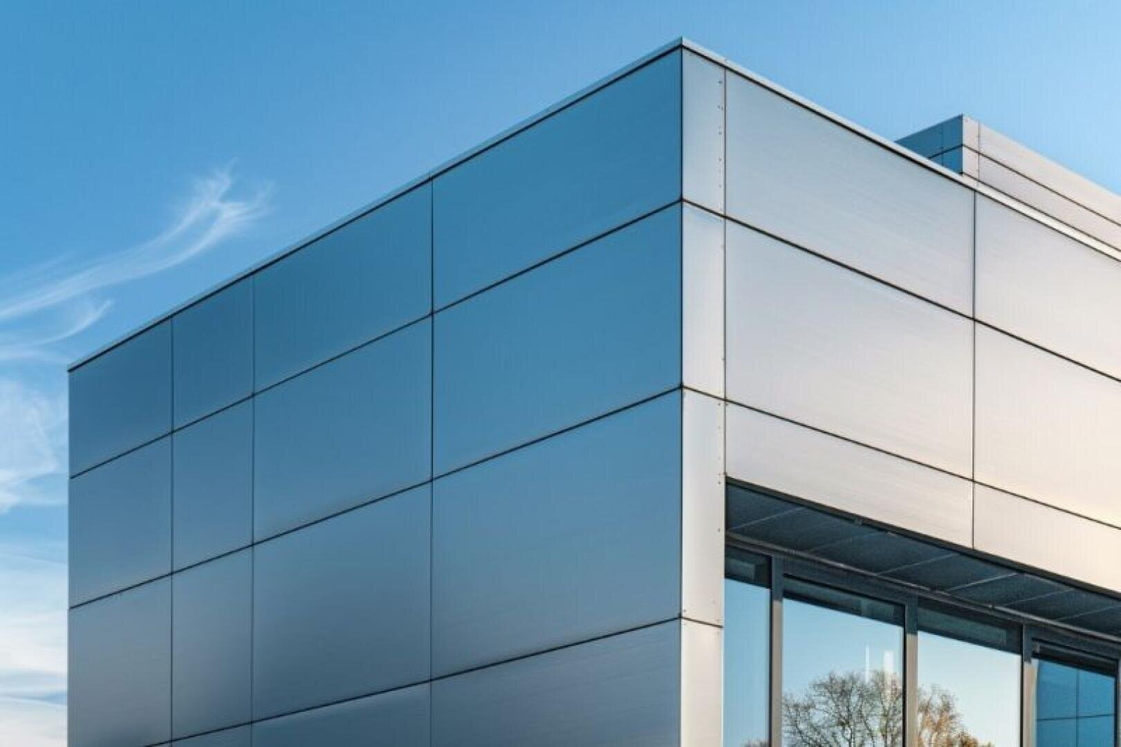 Modern building with a smooth, metallic façade and large reflective windows against a clear blue sky with wispy clouds.