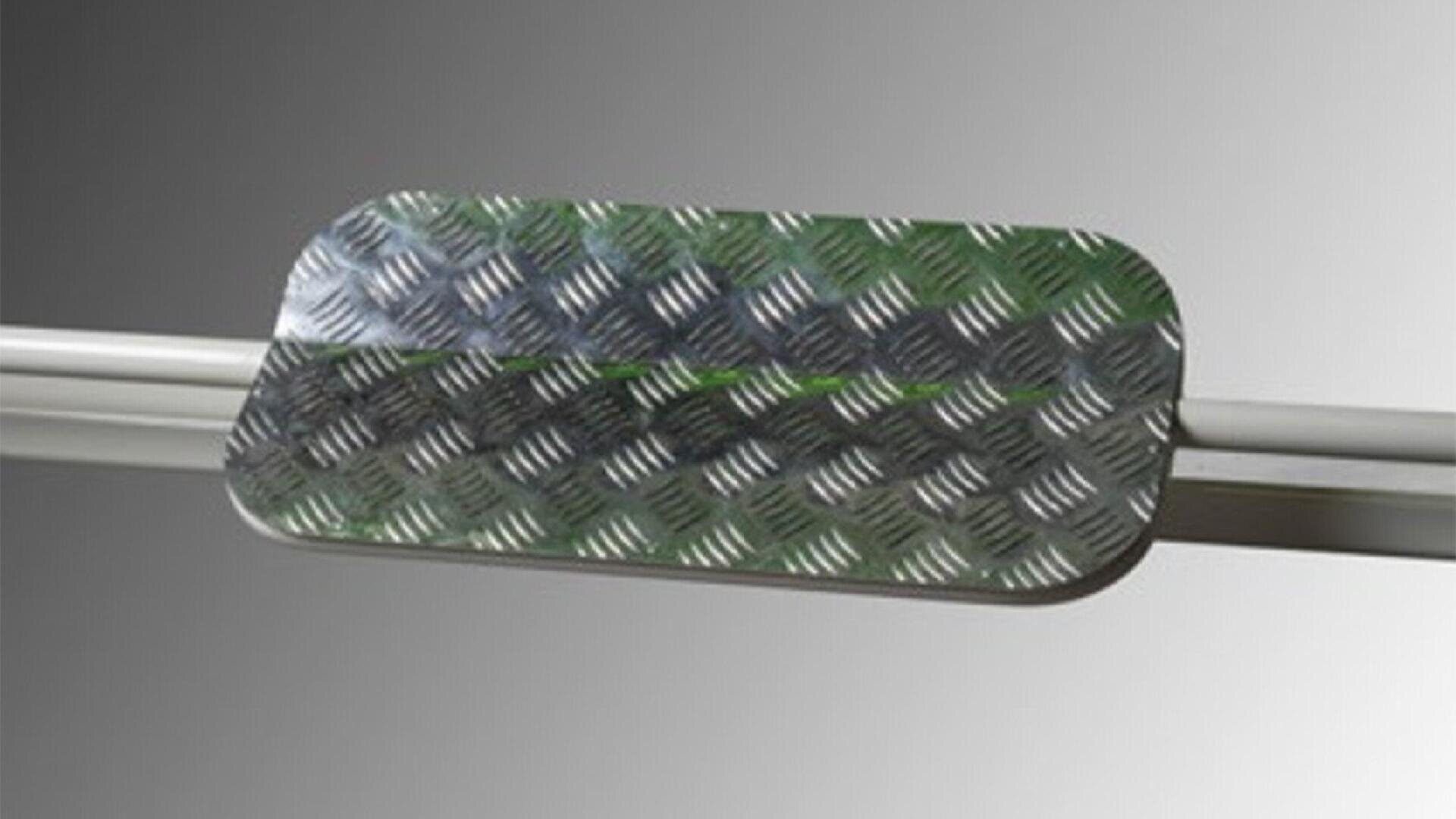 A rectangular metal plate with rounded corners and a raised diamond-pattern texture, mounted on a horizontal metal bar against a gradient gray background.