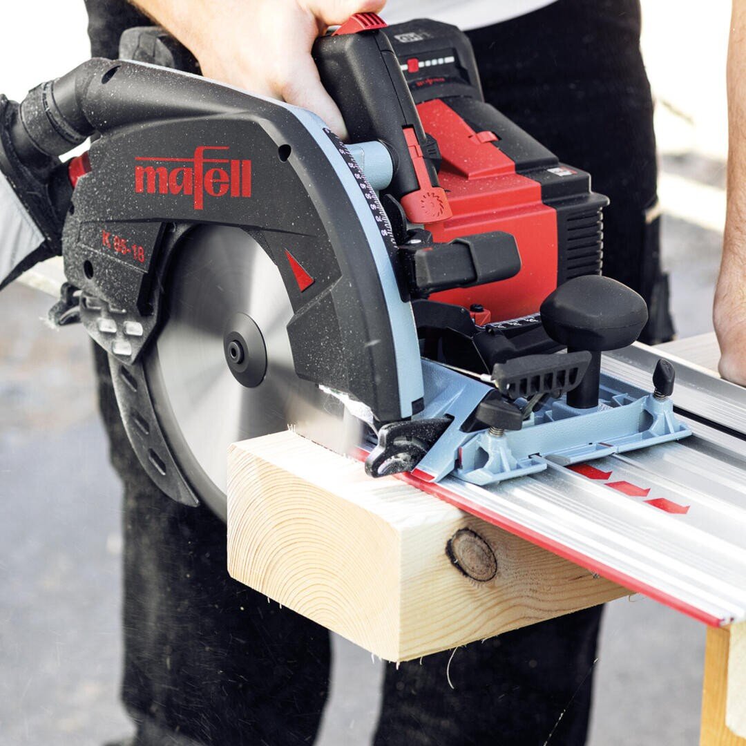 Eine Person schneidet mit einer Kreissäge der Marke Mafell durch einen Holzbalken und führt die Säge entlang einer Metallschiene, um einen präzisen Schnitt zu erzielen.