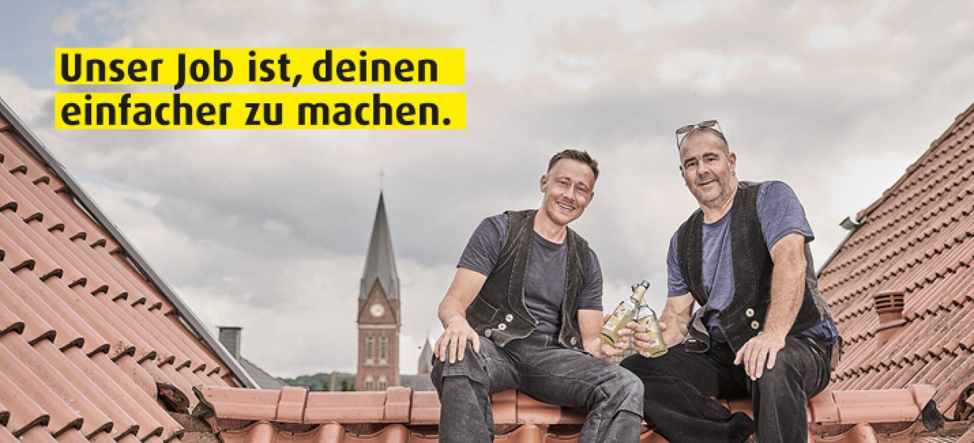 Zwei lächelnde Männer in Arbeitskleidung sitzen auf einem Kacheldach und halten Getränke in der Hand. Im Hintergrund ist ein Kirchturm zu sehen. Der Text auf Deutsch lautet: "Unser Job ist, deinen einfacher zu machen.".