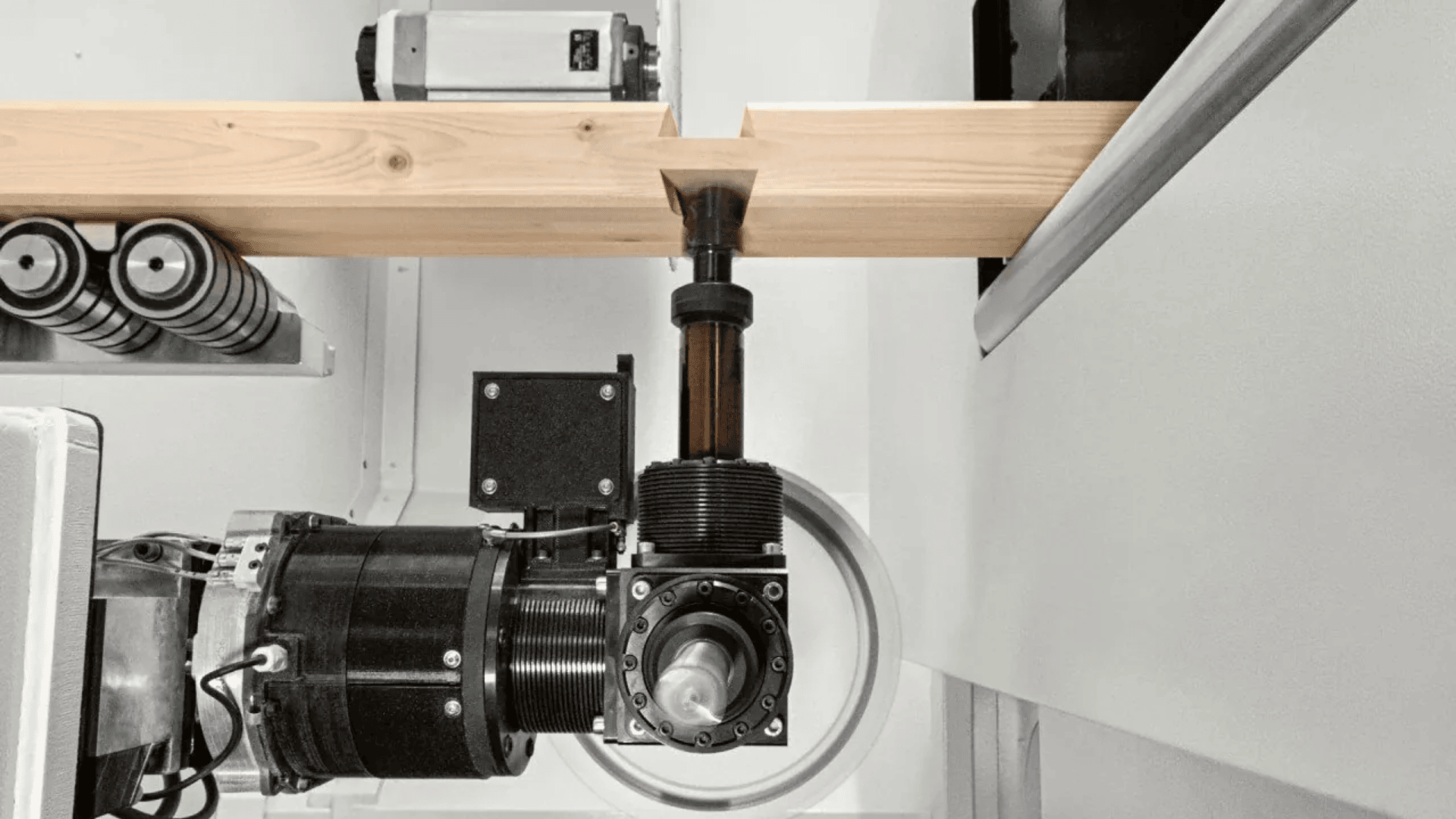 Eine Nahaufnahme einer CNC-Holzbearbeitungsmaschine, die eine präzise Kerbe in einen Holzbalken schneidet, wobei verschiedene mechanische Komponenten und Werkzeuge sichtbar sind.