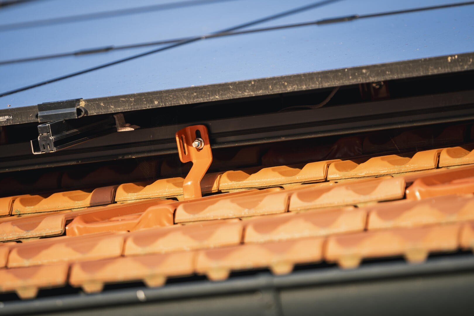 Nahaufnahme eines Daches mit orangefarbenen Ziegeln, die die Halterung und die Unterseite eines über den Ziegeln installierten Solarmoduls zeigt.