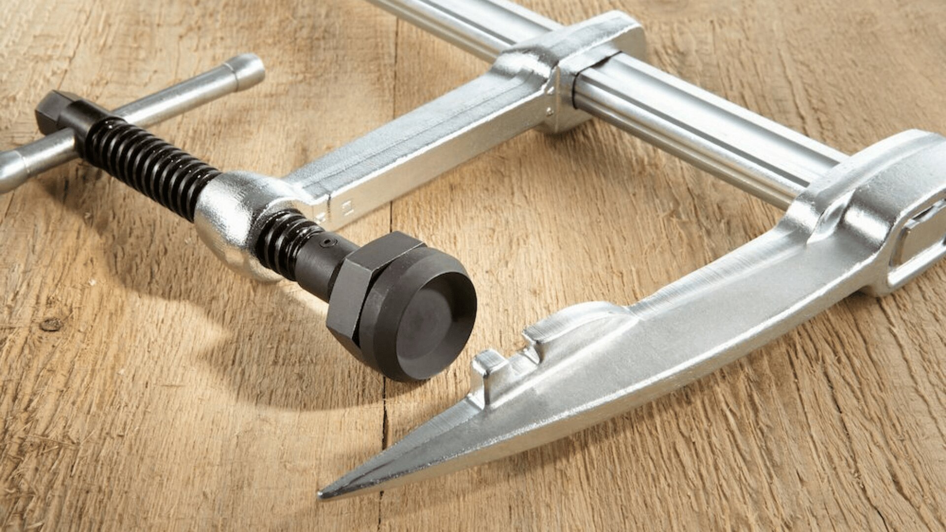 Eine Nahaufnahme eines silbernen Metallabziehwerkzeugs mit einem spitzen Arm und einem Schraubmechanismus, das auf einer Holzoberfläche ruht.