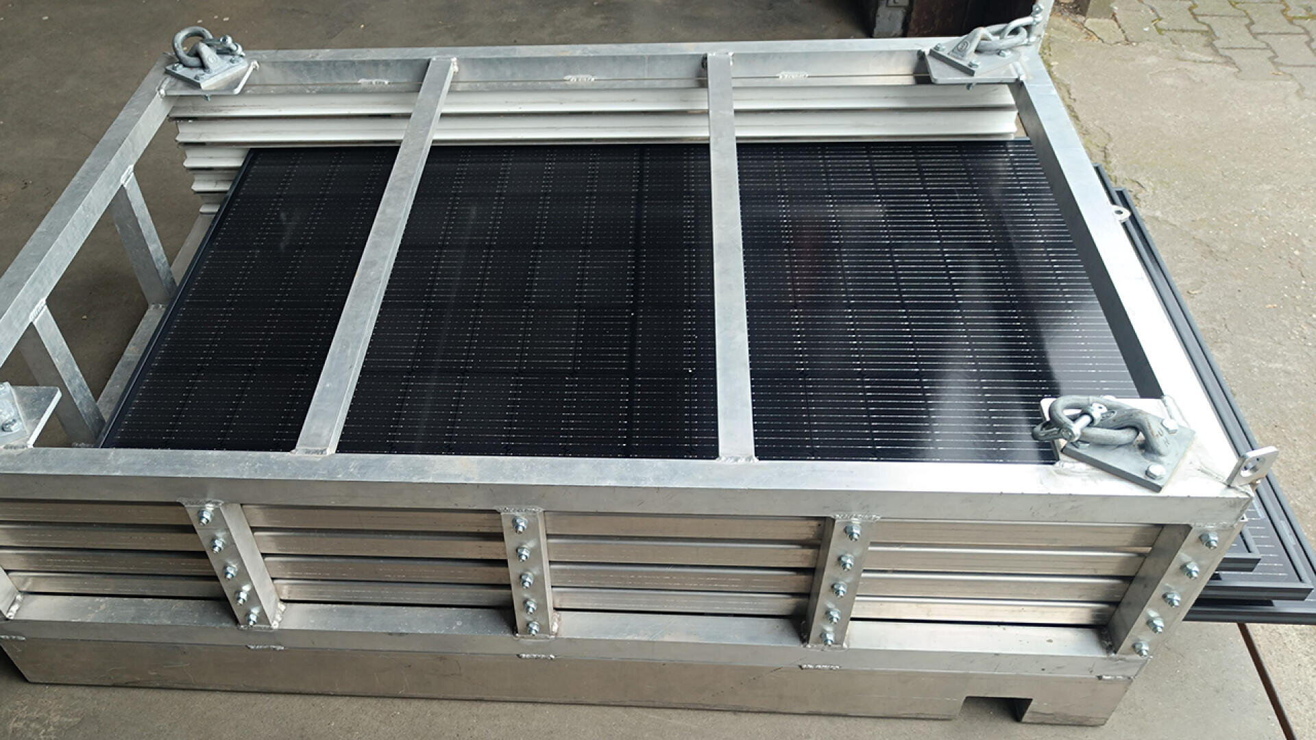 Ein Stapel Solarmodule, befestigt in einem stabilen Transportrahmen aus Metall, auf einem Betonboden platziert.