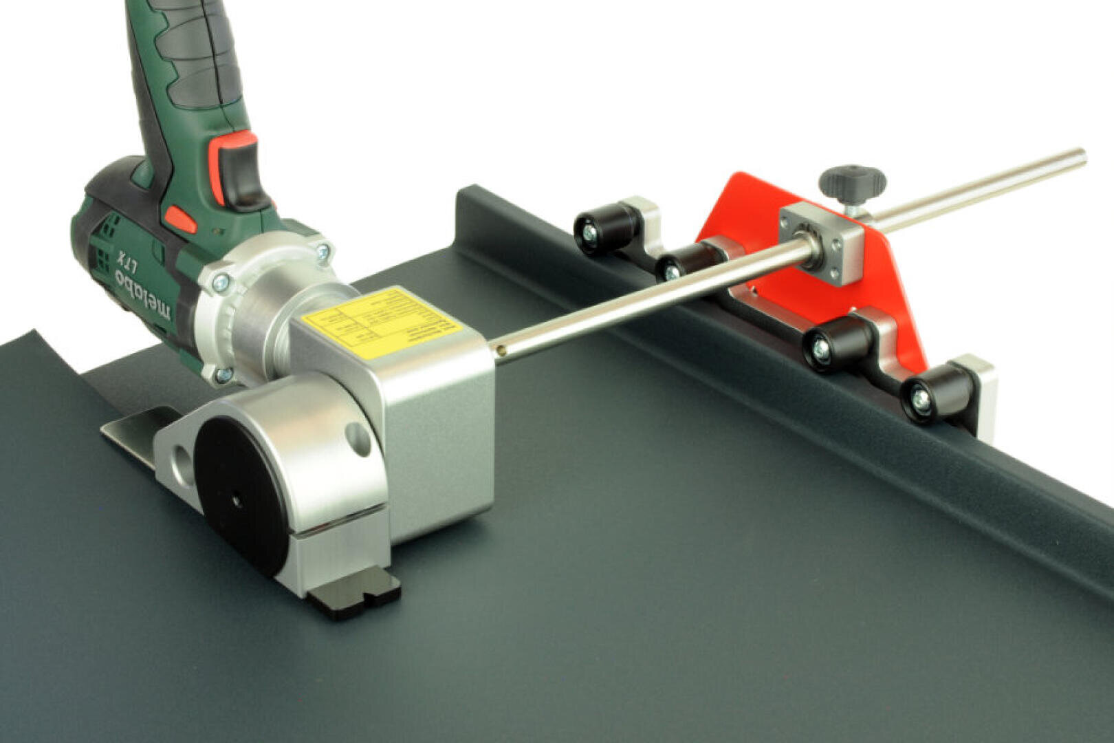 Close-up of a metal cutting tool with a green handle and yellow label, mounted on a dark, flat surface and aligned with a red and silver guide rail system.