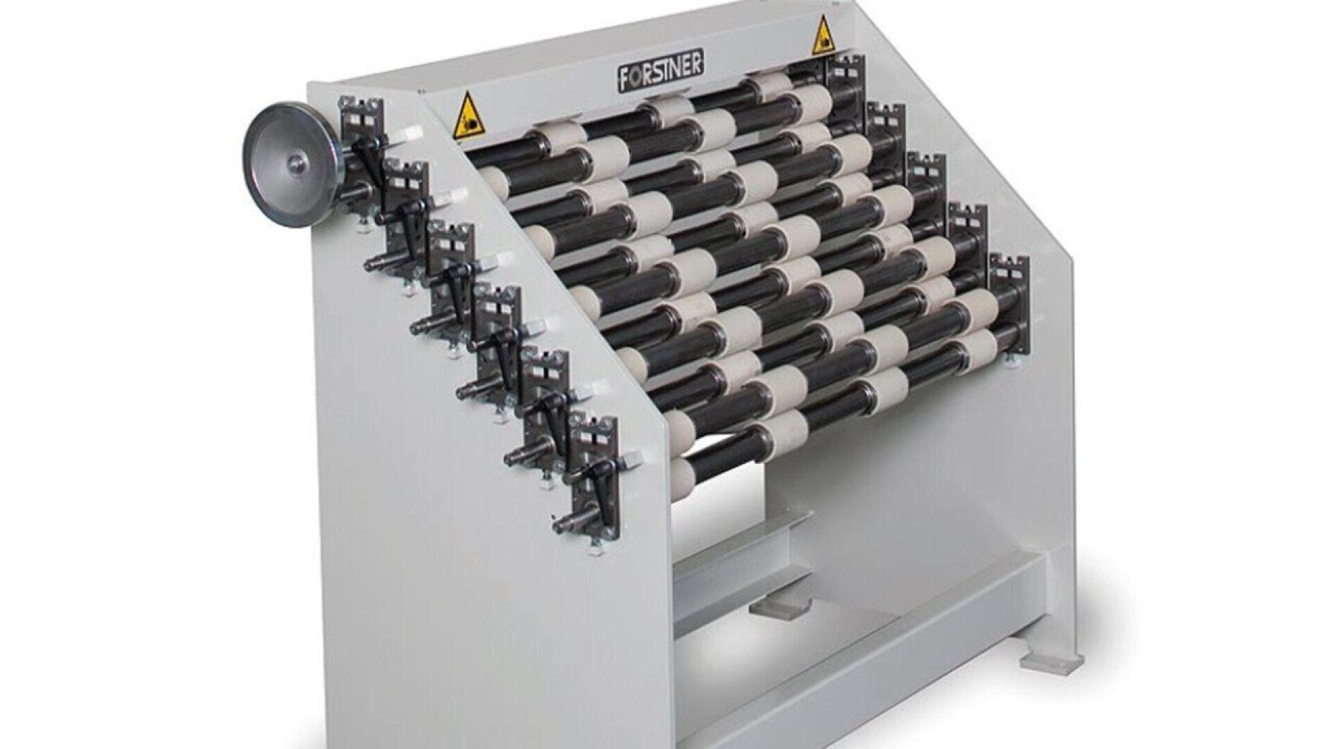 A metal slitting machine with multiple black and silver rollers arranged horizontally, used for cutting sheet metal into narrower strips. The machine is labeled FORSTNER and has visible adjustment knobs and warning signs.