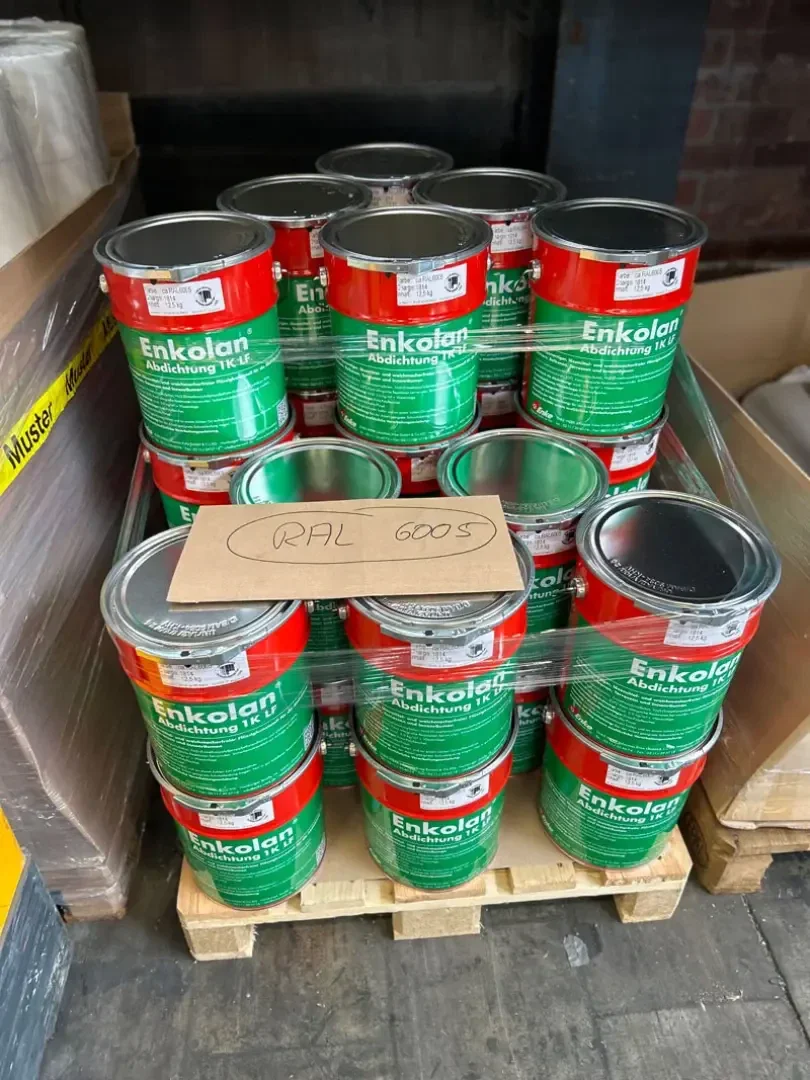 Mehrere Dosen Enkolan-Dichtmasse mit roten und grünen Etiketten sind auf einer Holzpalette gestapelt und in Plastikfolie eingewickelt. Auf den Dosen liegt ein Pappschild mit der Aufschrift RAL 6005.