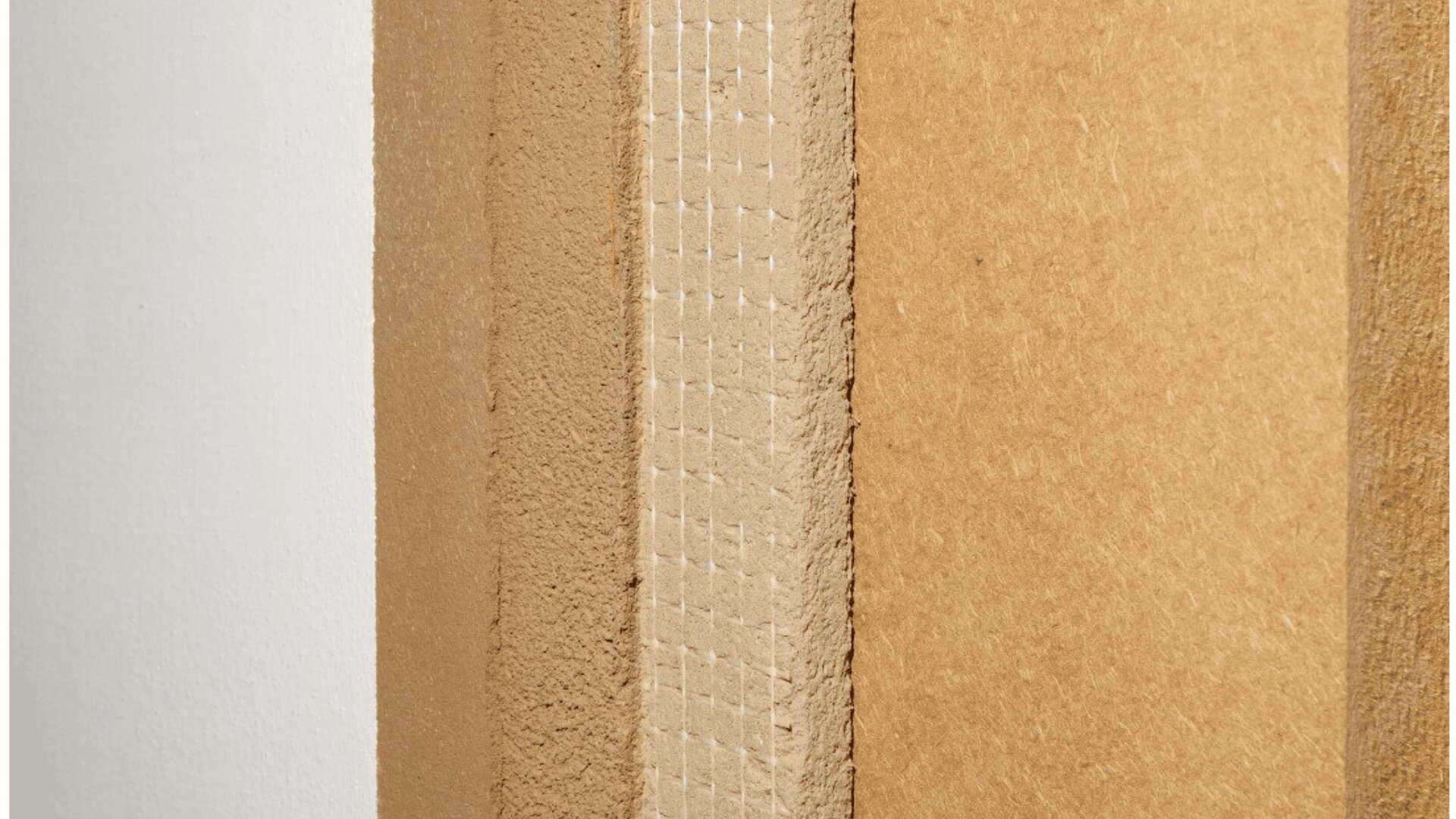 Close-up view of four stacked building material panels, showing different textures and layers, including smooth, fibrous, and grid-patterned surfaces in shades of beige and brown.