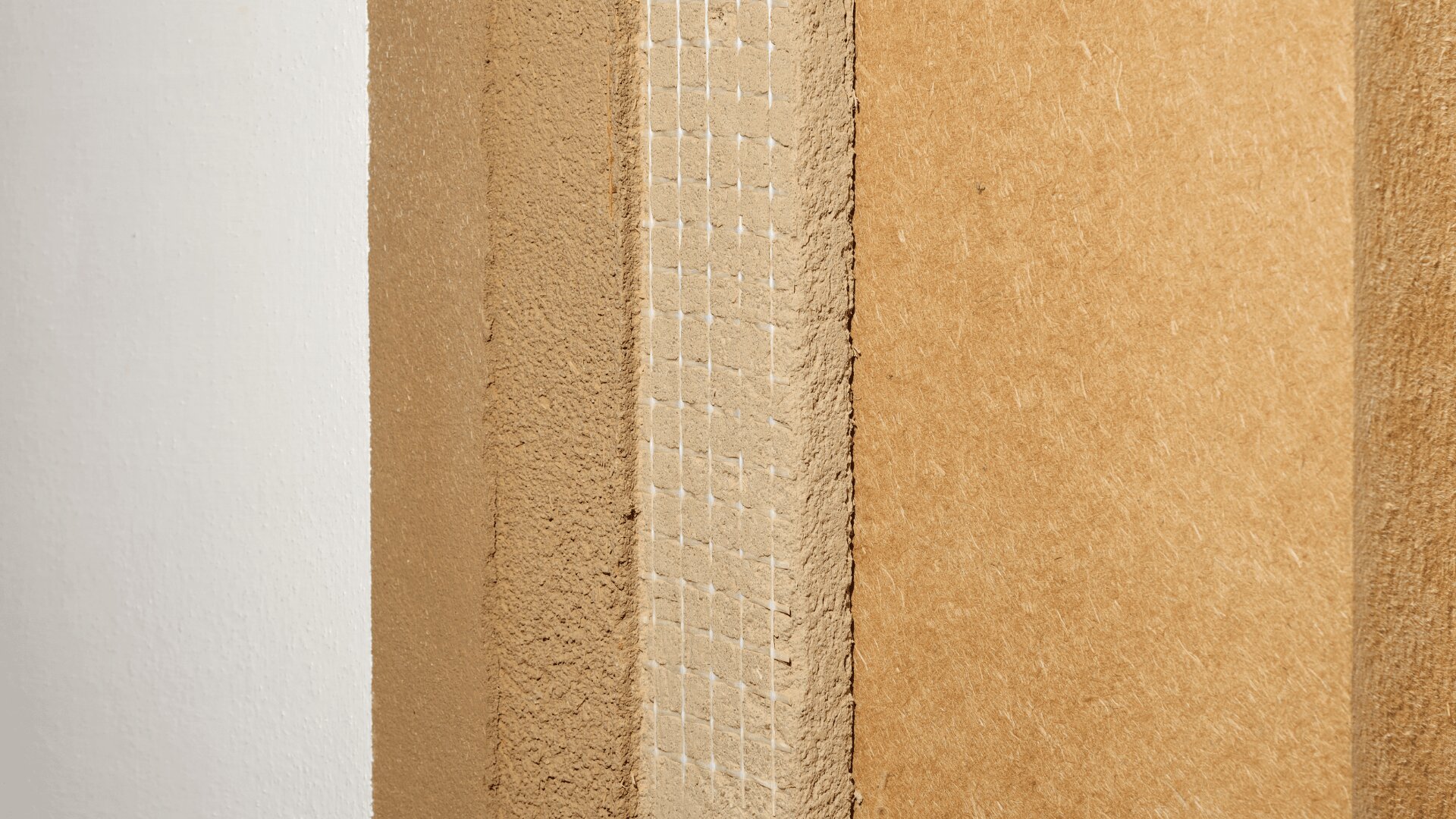Nahaufnahme der Kanten verschiedener Arten von Spanplatten oder MDF-Holzplatten, die ihre Texturen und Schichten zeigen und vertikal neben einer weißen Wand positioniert sind.