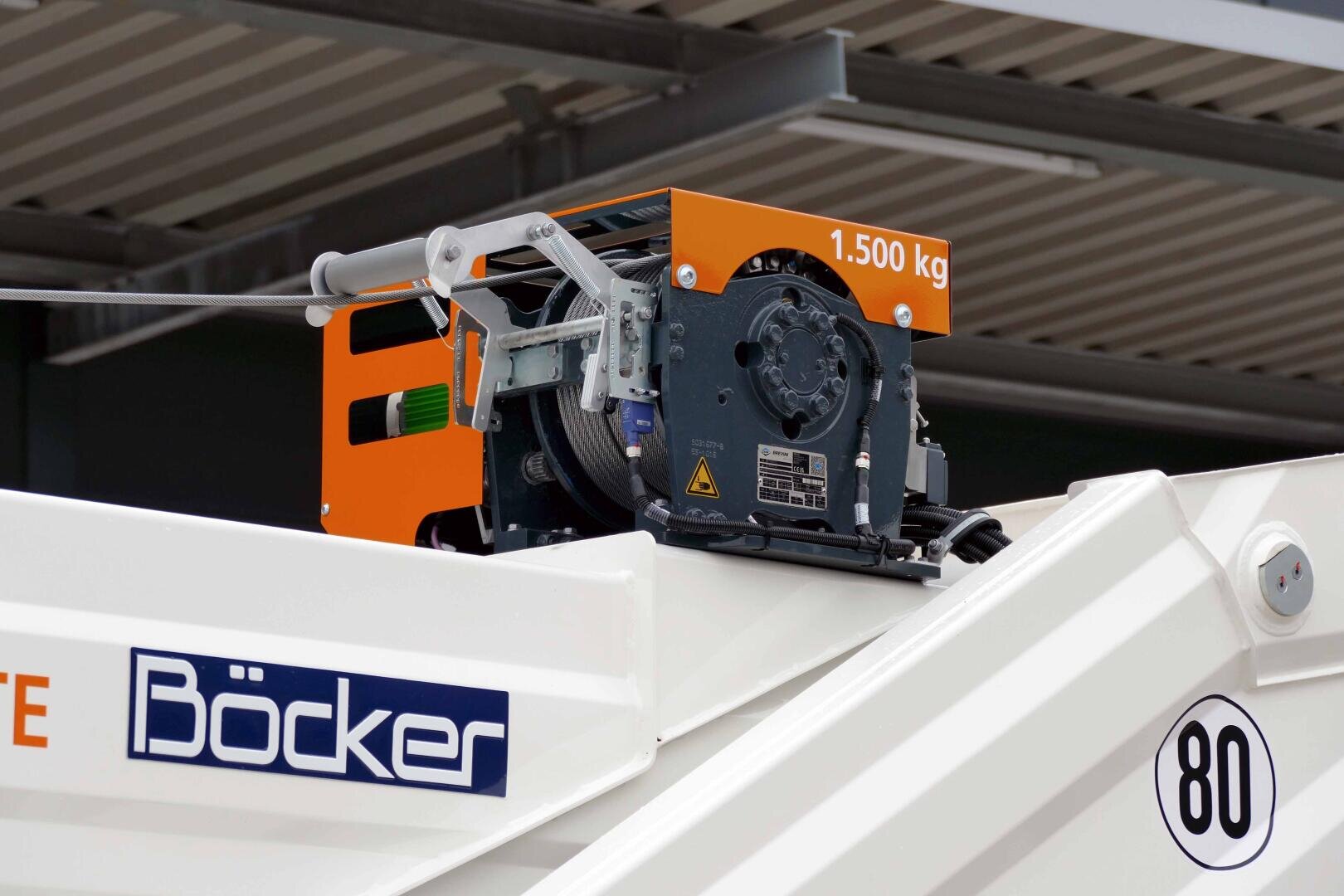 Close-up of a mechanical hoist with a weight of 1,500 kg, mounted on a white device with the brand name Böcker, under a metal roof construction.