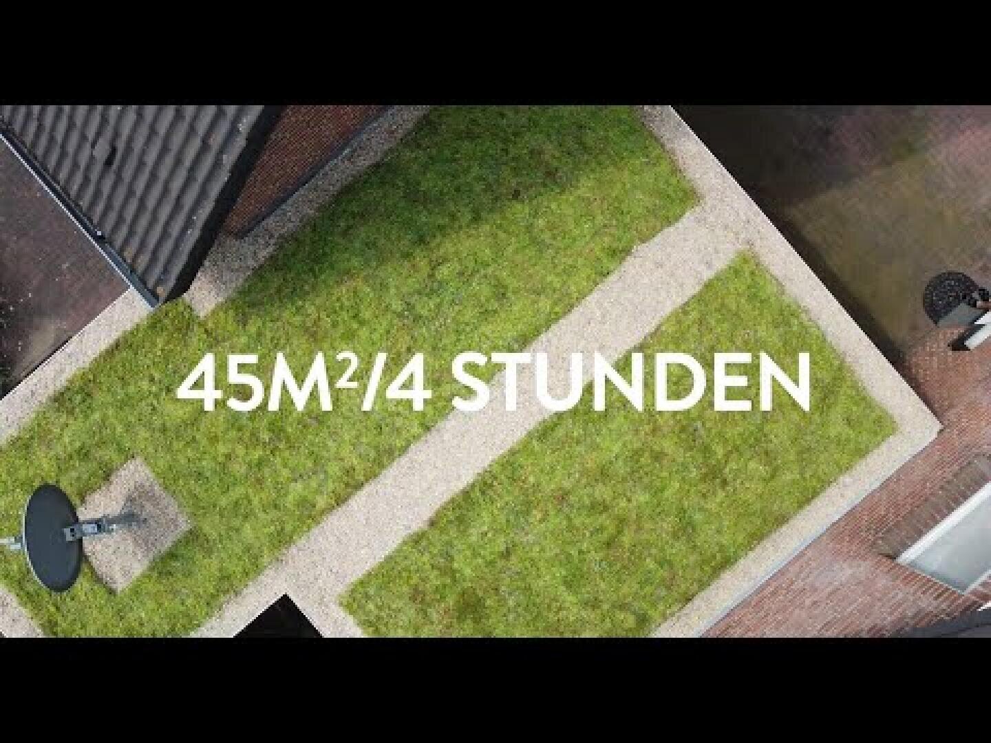Luftaufnahme einer rechteckigen, von Kieswegen gesäumten Rasenfläche, auf der in weißen Buchstaben der Text 45M²/4 STUNDEN eingeblendet ist. Teile von Dächern und eine Satellitenschüssel sind sichtbar.