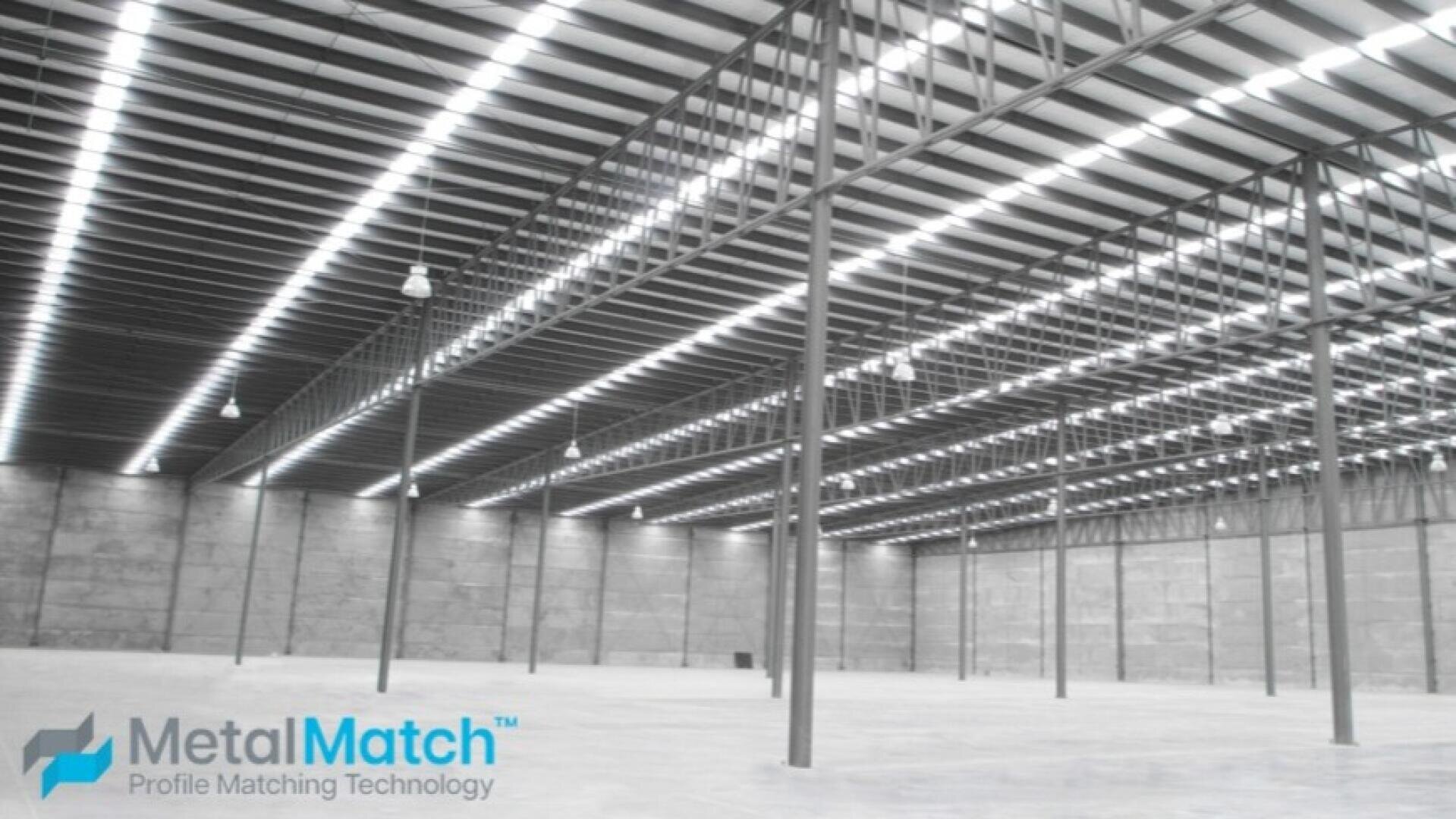 Eine große, leere Lagerhalle mit hohen Decken, Metallträgern und heller Deckenbeleuchtung. Der Boden ist aus Beton, und der Raum ist offen und geräumig. Das MetalMatch-Logo erscheint in der unteren linken Ecke.