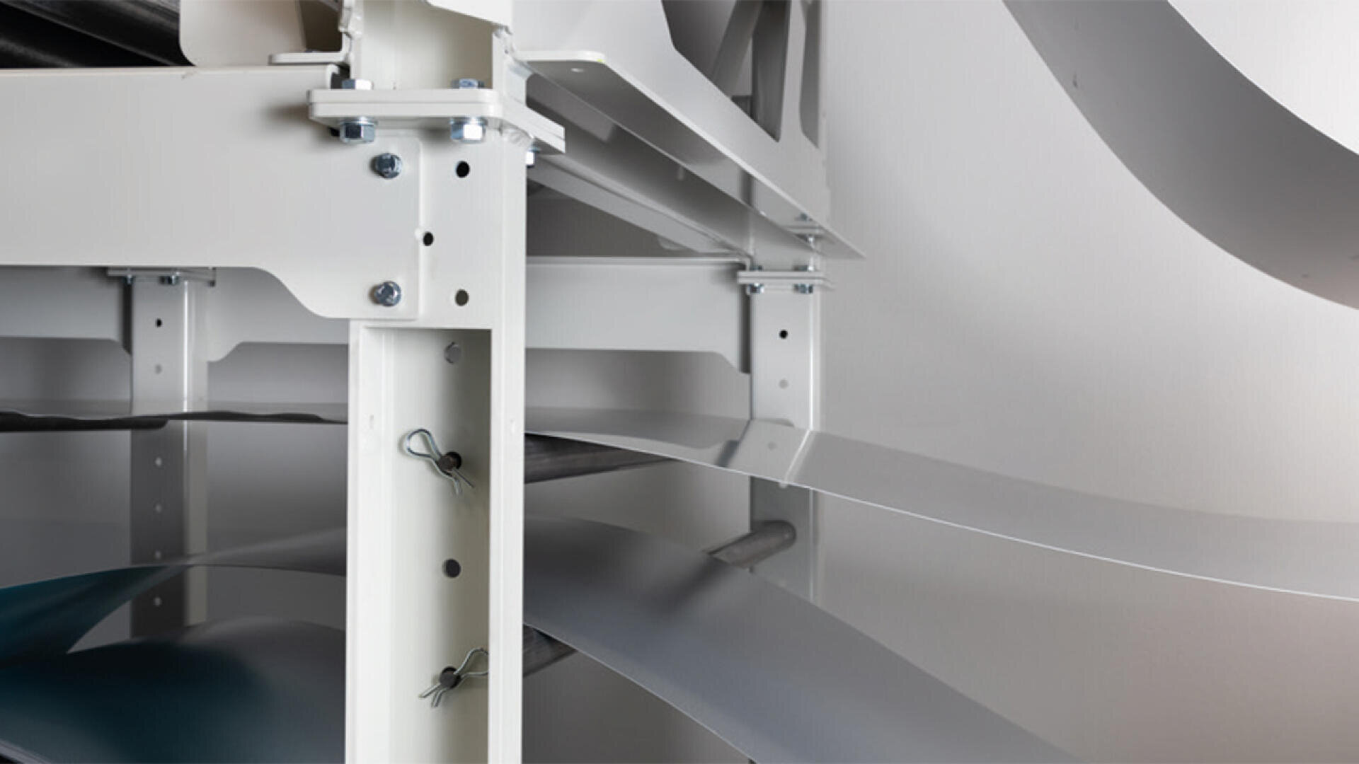 Nahaufnahme eines Metallregals mit gestapelten und teilweise ausgefahrenen dünnen Platten aus reflektierendem Metall oder Kunststoff, auf dem Bolzen, Stützbalken und Strukturdetails in einer industriellen Umgebung zu sehen sind.