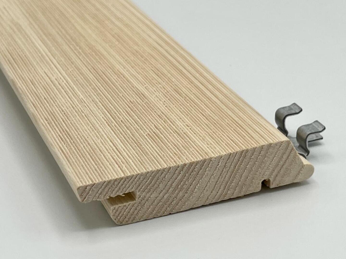Eine Nahaufnahme eines hellen Holzbretts mit einer geriffelten Kante und einer kleinen Metallklammer daneben, platziert auf einer weißen Oberfläche.