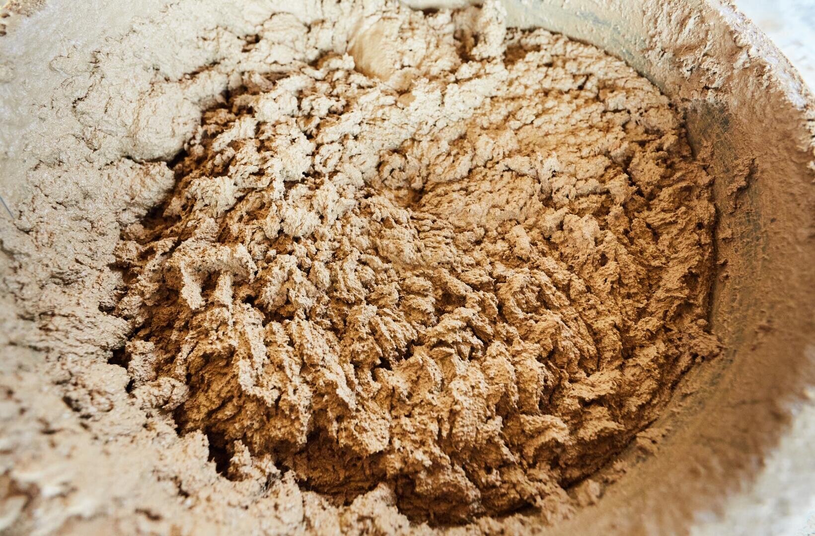 Eine Nahaufnahme einer Rührschüssel gefüllt mit trockenem, hellbraunem Pulver, wahrscheinlich Backzutaten wie Mehl und Kakaopulver, die teilweise miteinander vermischt sind.