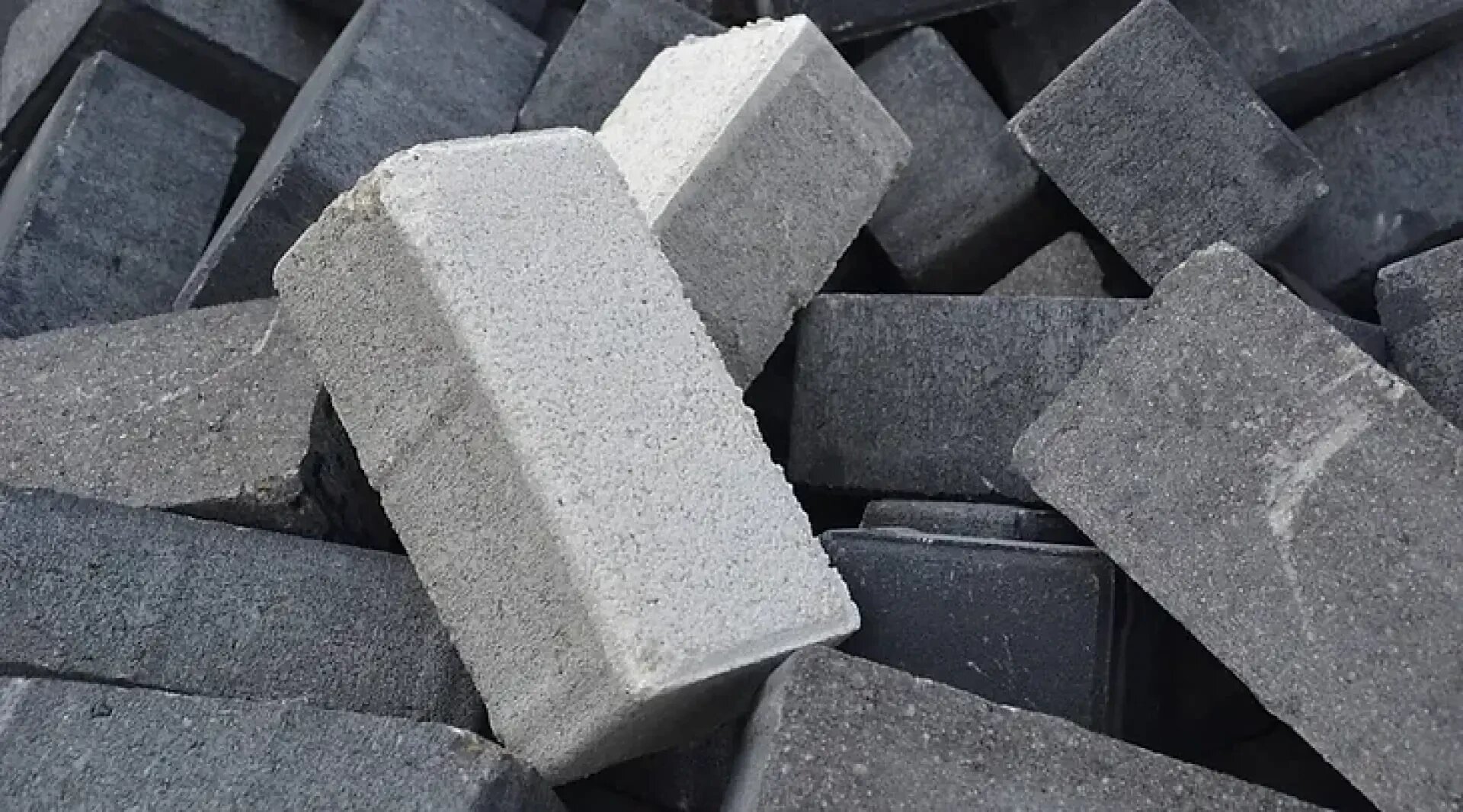 A pile of dark gray rectangular bricks with one lighter gray brick positioned diagonally on top, standing out from the rest.