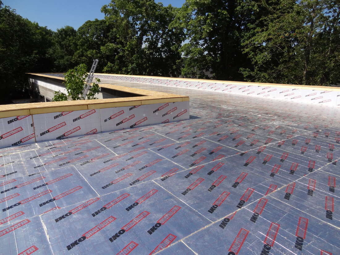 Im Bau befindliches Flachdach mit Dämmstoffplatten mit der Bezeichnung IKO Enertherm, die die Oberfläche bedecken; im Hintergrund sind Bäume und eine Leiter zu sehen.